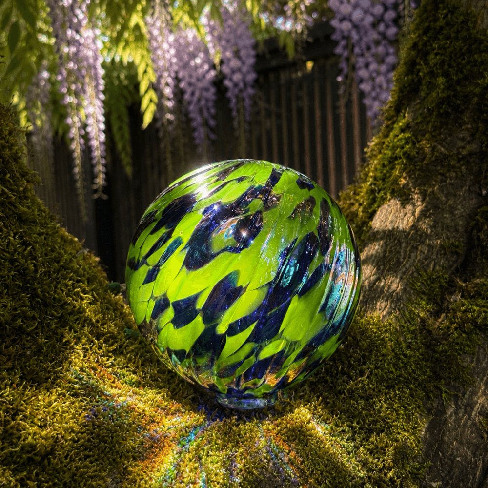 Sunday Blue glass float showcasing vibrant green and blue swirls, reflecting light in a natural setting.