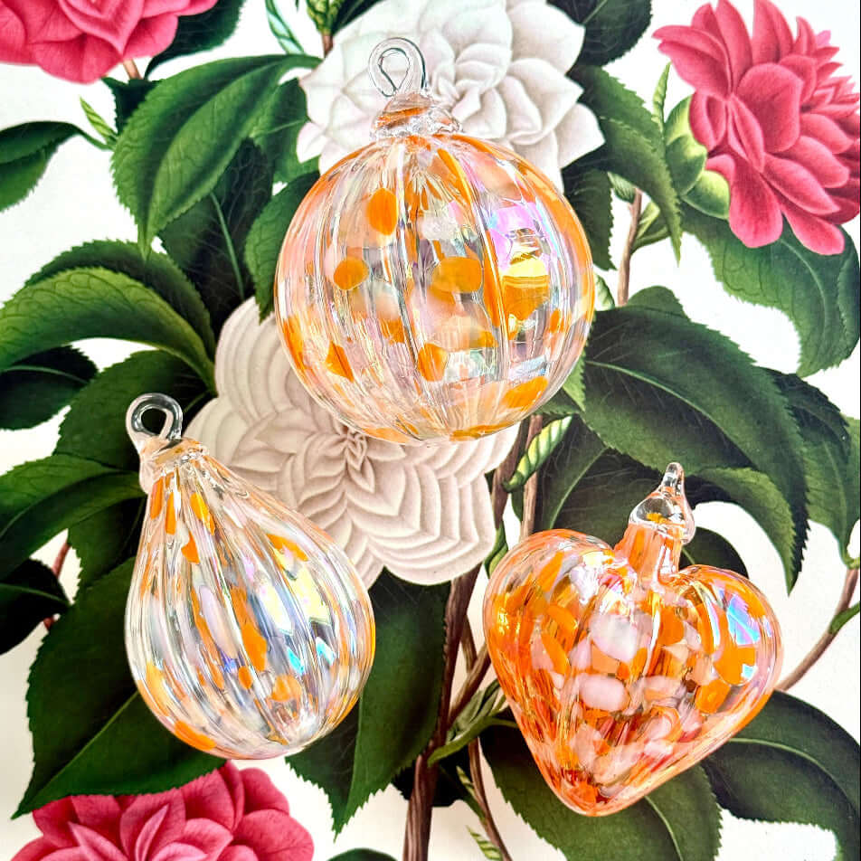 Colorful glass ornaments in Salmonberry hues on floral background, part of the Lacey Special Edition Collection.