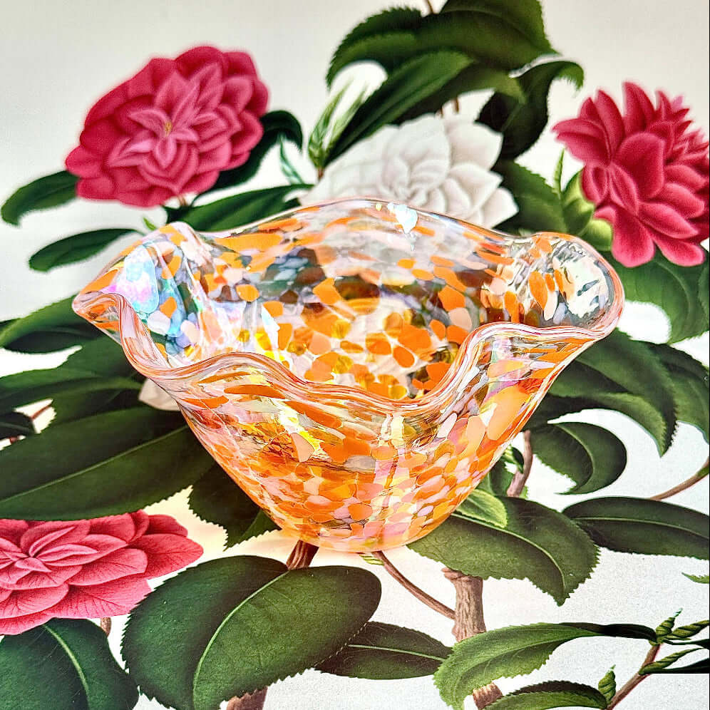 Handmade Salmonberry wave bowl featuring an iridescent finish in amber and orange on a floral background.